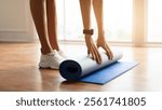 Stay Fit Concept. Closeup Cropped View Of Young Woman In White Sneakers Rolling Yoga Mat Practicing Pilates At Home Excercising In Living Room Or At Fitness Studio, Wearing Smartwatch