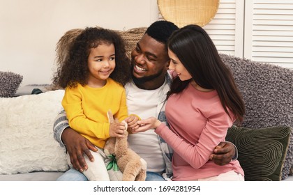 Stay at home concept. African american dad and european mom are looking at daughter sitting on couch