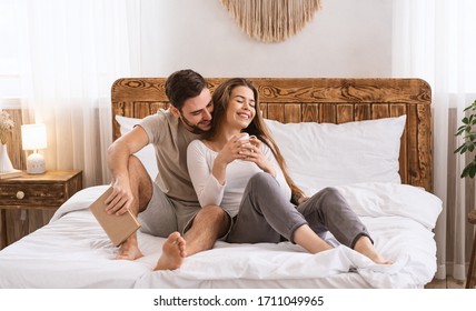 Stay at home concept. Guy with book, girl with cup on bed