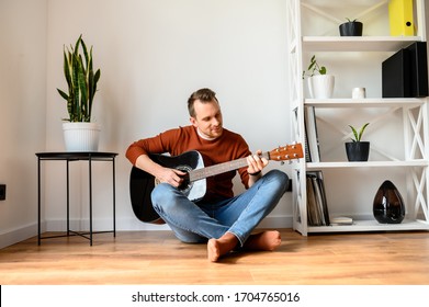 Stay Home. A Guy Spends His Leisure Time At Home Playing Music. He Is Sitting On A Cozy Plaid With An Acoustic Guitar In His Hands.