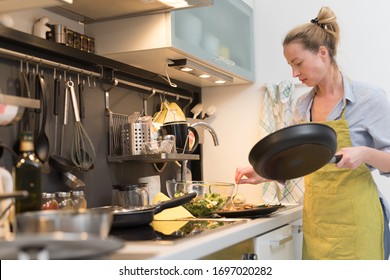 Stay At Home Housewife Woman Cooking In Kitchen, Salting Dish In A Saucepan, Preparing Food For Family Dinner. Blonde Caucasian Model In Her 30is, Real Cooking Not Looking In Camera.