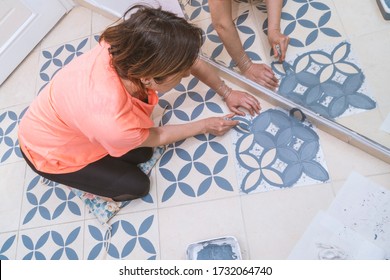 Das Konzept der Heim- und Wohnungsverbesserung: Die obere Ansicht einer Frau Malerei mit einer Bürste eine dekorative Vorlage auf Bodenfliesen in Grau durch Verwendung eines generischen türkischen Muster Schablone. Spiegelreflektion