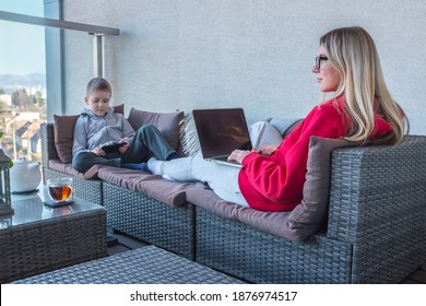 Stay At Home Mom. Mother And Son Spend Free Time On Terrace. Woman Working, Child Using Smartphone. Weekend Family. Bonding Concept.