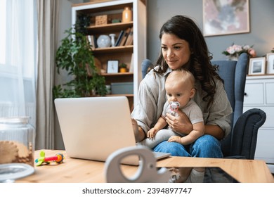 Stay at home mom working remotely on laptop while taking care of her baby. Young business mother on maternity leave trying to freelance by the desk with toddler child. Global work on computer - Powered by Shutterstock