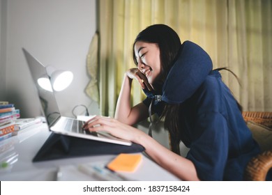 Stay At Home Office Lifestyle Concept. Young Adult Freelancer Asian Woman Using Laptop Wear Neck Pillow In Workplace Space On Night Shift. Still Life With Modern Digital Online Media.