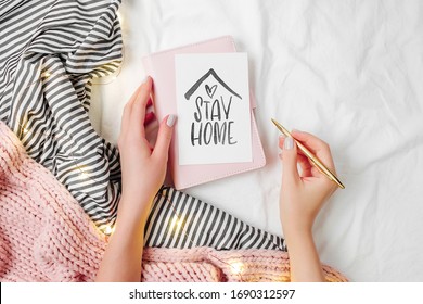 Stay Home, quarantine. Working From Home. Female hands hold warning poster.  Bedding sheets with fairy lights. Copy space. Flat lay, top view