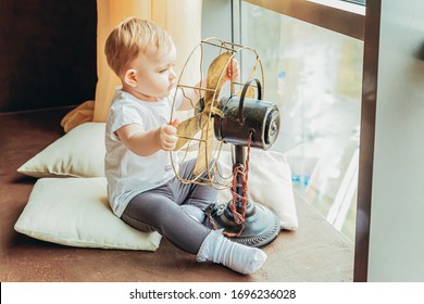 Stay Home Stay Safe. Little Cute Sweet Infant Little Baby Girl Sitting With Ventilator Fan Near Large Window In Bright Light Living Room At Home Indoors. Childhood Family Maternity Tenderness Concept