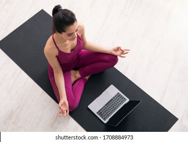 Stay Home Yoga. Young Woman In Lotus Pose Following Online Meditation On Laptop, Top View. Mockup For Design