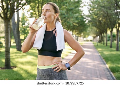 Stay hydrated. Tired fit woman in sportswear refreshing, drinking water after jogging in a green park on a sunny day - Powered by Shutterstock