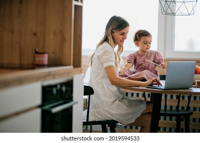 Stay At Mother Home Sitting In Kitchen And Getting Work Done While Her Baby Girl Helping Her.