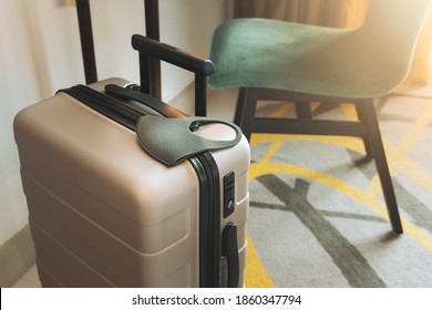 Stay Safe While Travel During Covid 19 Pandemic Concept. A Suitcase Or Baggage With A Medical Face Mask In The Hotel Room. Travel Bubbles, Business Trip, ASQ Alternative State Quarantine, New Normal.