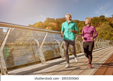 Stay in shape. Full length shot of active mature family couple in sportswear smiling at each other while jogging together on a sunny autumn day. Joyful senior couple doing sport outdoors