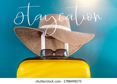 Staycation Word. Bright And Stylish Cabin Size Suitcase With Straw Hat Against Bright Blue Background. Easy Travel At Home Country During Coronavirus Outbreak With Little Baggage Concept.