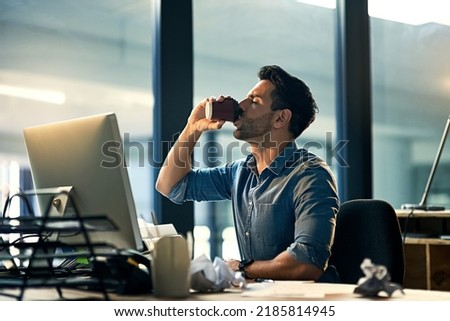 Staying awake at work with a caffeine boost. Shot of a young businessman drinking coffee during a late night at work.