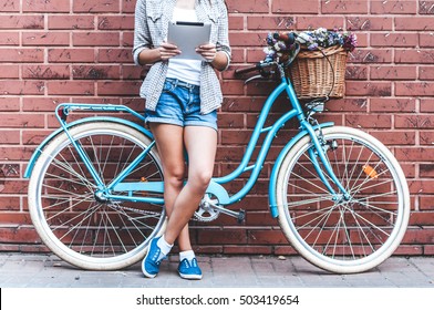 Staying connected with social media. Close-up of young attractive woman holding tablet  while leaning at she's bicycle with wall in the background - Powered by Shutterstock