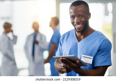 Staying Current Is An Important Part Of My Job. Portrait Of A Young Doctor Using A Digital Tablet With His Colleagues In The Background.