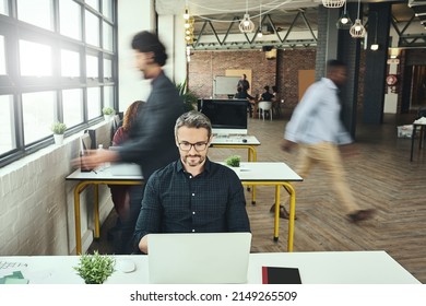 Staying Focused Amidst The Hustle And Bustle. Cropped Shot Of A Mature Businessman Working On His Laptop In The Office.