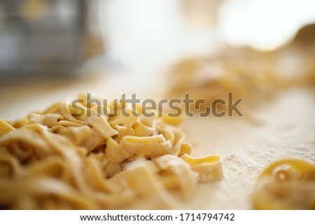 Staying at home with your family and preparing fresh home-made pasta (tagliatelle): mom creating nests of pasta noodles on a wooden board.