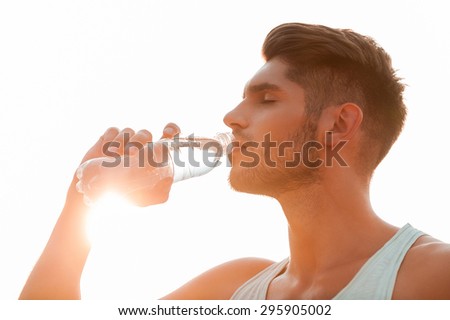 Staying hydrated. Low angle view of young man drinking water and keeping eyes closed while standing outdoors