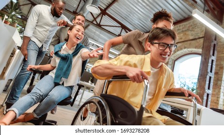 Staying Positive. Young Happy Asian Man In Wheelchair Having Fun With His Colleagues At Modern Office. Disability Concept. Office Fun