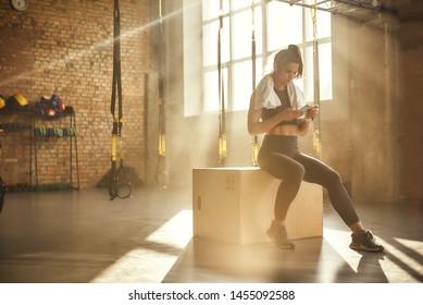 Staying in touch. Attractive athletic woman in headphones wearing towel on her shoulders and using smart phone while sitting at gym - Powered by Shutterstock