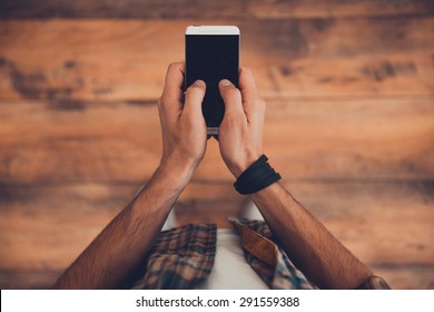 Staying In Touch. Top View Of Man Holding Smart Phone While Standing On The Wooden Floor 