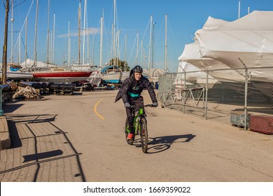 St.Catharines, Canada- 03/09/2020; A Teenager Rides A Bicycle In A Strong Wind.  Winter Boat Storage Near Lake Ontario.