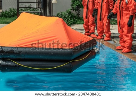 stcw maritime training, basic safety on water, seafarers or sailors opening life raft in the pool wearing waterproof suits