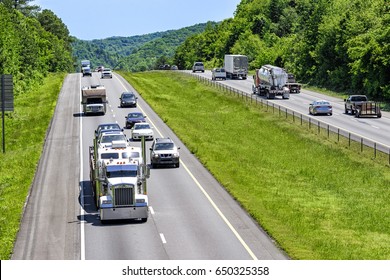 A steady mix of trucks, cars and SUVs roll down an interstate highway in eastern Tennessee.  Heat rising from the pavement gives a cool shimmering effect to vehicles and forest in the distance.