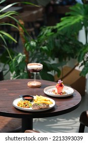 Steak On Plate, A Plate Of Panna Cotta, And Drink In Tall Glass. Food And Drink On The Table. Plant In Pot As Background. Steak, Panacota Dan Minuman Di Meja.