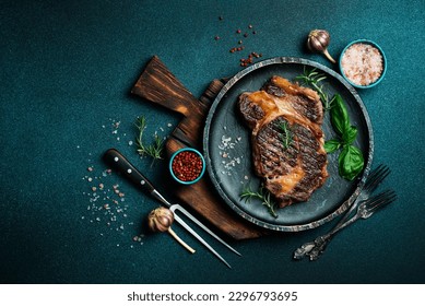 steak ribeye, grilled with pepper, garlic, salt and thyme served on a cutting board on a dark stone background. Top view with copy space. Flat lay