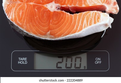 Steak of salmon fish in a black plate on digital scale displaying 200 gram.