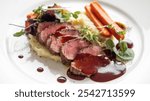 Steak: A sliced steak with red sauce, accompanied by roasted carrots, mashed potatoes, and fresh greens, elegantly plated for a fine dining experience.