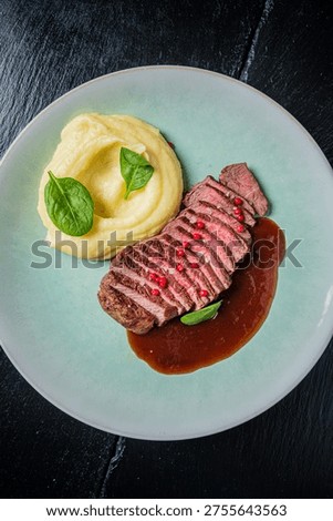 Steak slices atop smooth mashed potatoes, drizzled with sauce and fresh greens.