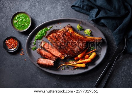 Steak tomahawk on a bone with roasted carrots and chimichurri sauce on a plate. Dark background. Close up. Top view.