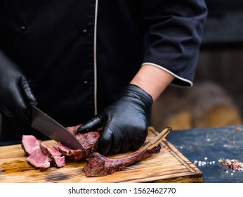 Steakhouse Kitchen. Cropped Shot Of Chef Serving Cowboy Steak, Slicing Grilled Beef Meat On Wooden Board.