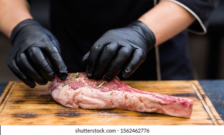 Steakhouse Kitchen. Cropped Shot Of Chef Cooking Cowboy Steak, Seasoning Raw Beef Bone In Meat On Wooden Board.