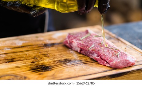 Steakhouse Kitchen. Cropped Shot Of Chef Cooking Cowboy Steak, Pouring Oil Over Raw Beef Bone In Meat On Wooden Board.