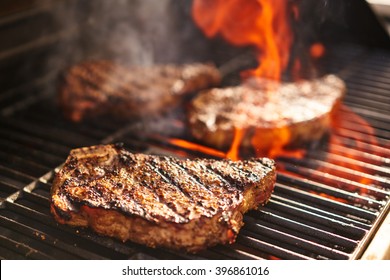 steaks cooking over flaming grill