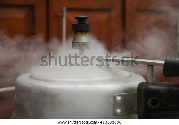 Steam\
escaping from lid of pressure cooker with reflection of modern\
kitchen. Indian style cooking rice or dhal\
