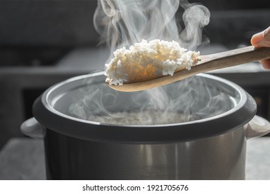 The steam from  Hand hold wooden ladle in electric rice cooker in the kitchen.hot food concept