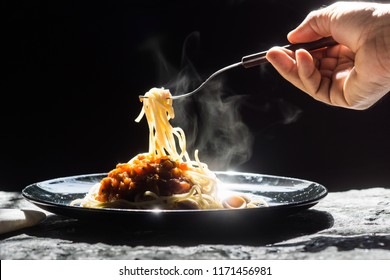 The steam from hand holding Spaghetti on a fork. Pasta with fresh tomatoes and herbs