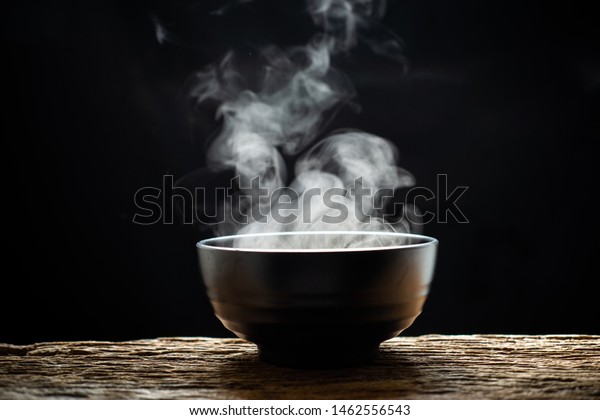 Steam of hot soup with smoke wood\
bowl on dark background.selective focus.hot food\
concept