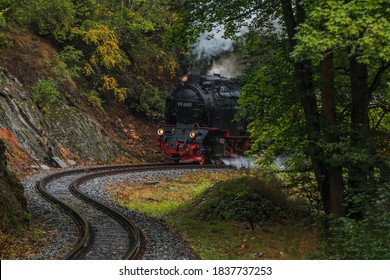 Steam locomotive in a valley in the Harz Mountains. Narrow gauge railway in the mountains in rainy weather in autumn on a track. Trees and rock face along the railroad tracks - Powered by Shutterstock