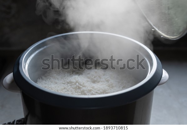 The steam from A man hand
lifting a glass lid off electric rice cooker in the kitchen.hot
food concept