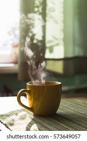 Steam of morning tea above yellow cup on table