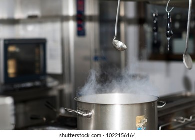 Steam Over Cooking Pot In Kitchen On Dark Background, Inox Ladle Hanging From Above The Stove
