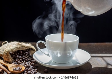 The steam from Pouring coffee into cup , A cup of fresh coffee on old kitchen table. with copy space. A scattering of coffee beans with a cup of coffee. Coarse fabric ,hot food and healthy meal concep