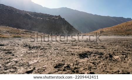 Steam rises from the ground in the mountains. The place resembles a volcano. Steep cliffs and cliffs. There is yellow grass on the slopes. Various traces are visible. The sun is shining brightly