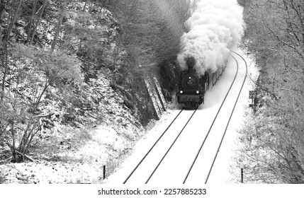 Steam train on the “Ruhrtalbahn“ (Ruhr valley line) between Arnsberg and Meschede Sauerland Germany heading to Winterberg. Engine with big puff of smoke on snowy winters day, black and white greyscale - Shutterstock ID 2257885233